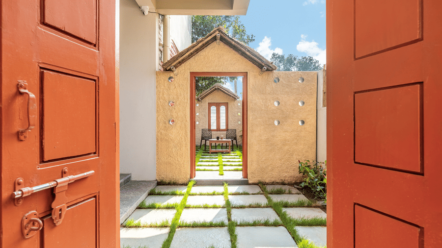 View through an open orange door into a private stone-and-grass tiled courtyard - Nature Trails Ashoka Resort Hampi