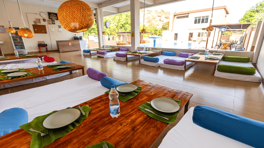 Large open-air dining area with low wooden tables set with banana leaves and colourful floor seating - Nature Trails Ashoka Resort Hampi