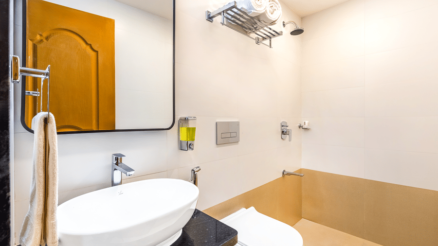 A white vessel sink sits on a black countertop with a sleek chrome faucet. Above it hangs a large, rectangular mirror with rounded corners, reflecting a light-colored wooden door at Nature Trails Durshet.