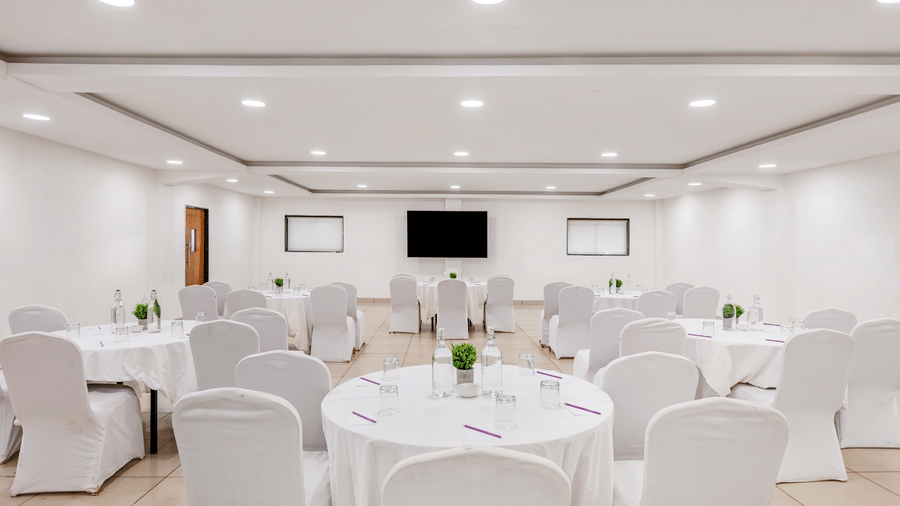 Bright conference room at Nature Trails Durshet with round tables, white chair covers, a wall-mounted TV, and recessed lighting.