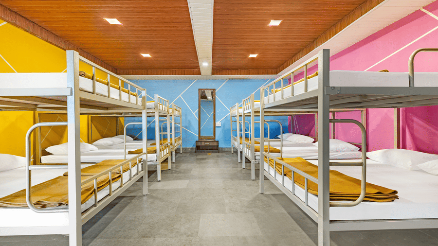 Nature Trails Kudalika 20 dom room bunk bed closeup with white bedding, mustard blanket, metal frame and pink geometric feature wall with white line pattern.