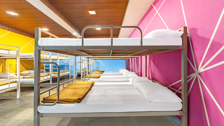 Nature Trails Kudalika 20 dom room full-length view with metal bunk beds, white bedding, mustard blankets, full-length mirror, yellow and pink geometric walls.