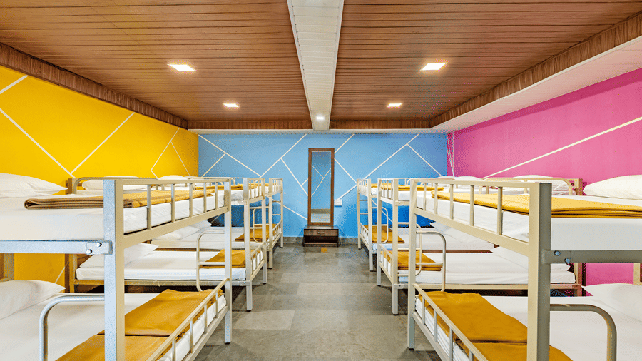 Nature Trails Kudalika 20 dom room with metal bunk beds, white bedding, mustard blankets, full-length mirror on blue feature wall, yellow and pink painted walls.