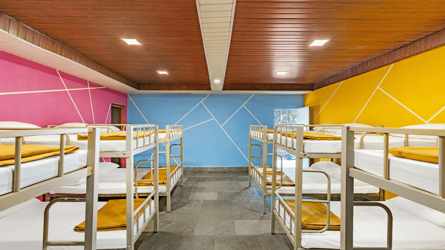 Nature Trails Kudalika 20 dom room with rows of metal bunk beds, white bedding, mustard blankets, pink blue and yellow geometric walls and wood-panelled ceiling.
