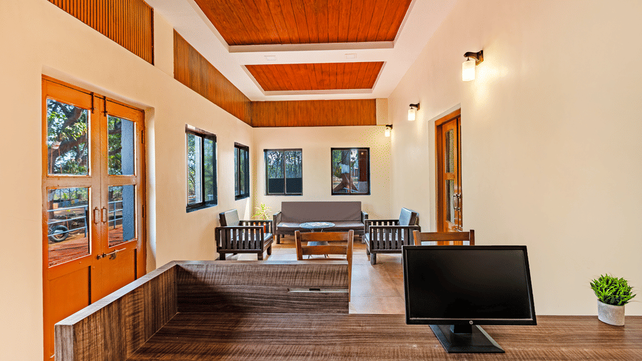 Nature Trails Kudalika reception desk with computer, wooden counter, lounge seating area, wood-panelled coffered ceiling, wall lights and wooden entrance doors.