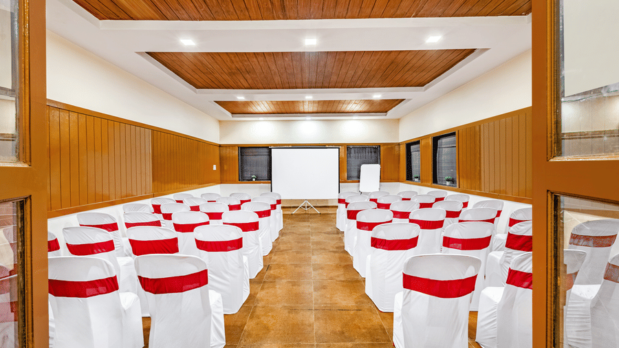 Nature Trails Kudalika conference hall entrance view with theatre-style white and red chairs, projection screen, wooden panelling and coffered ceiling.