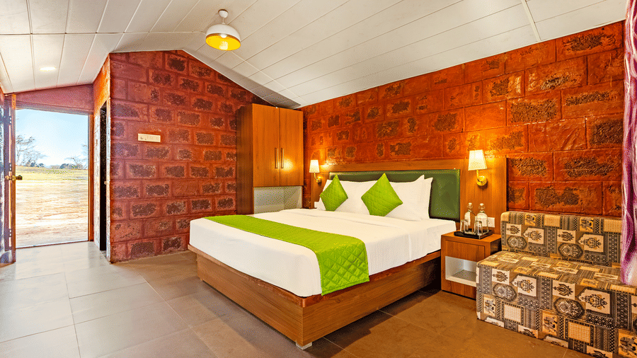 Nature Trails Kundalika – Deluxe room with king bed, green accents, and red brick wall decor.