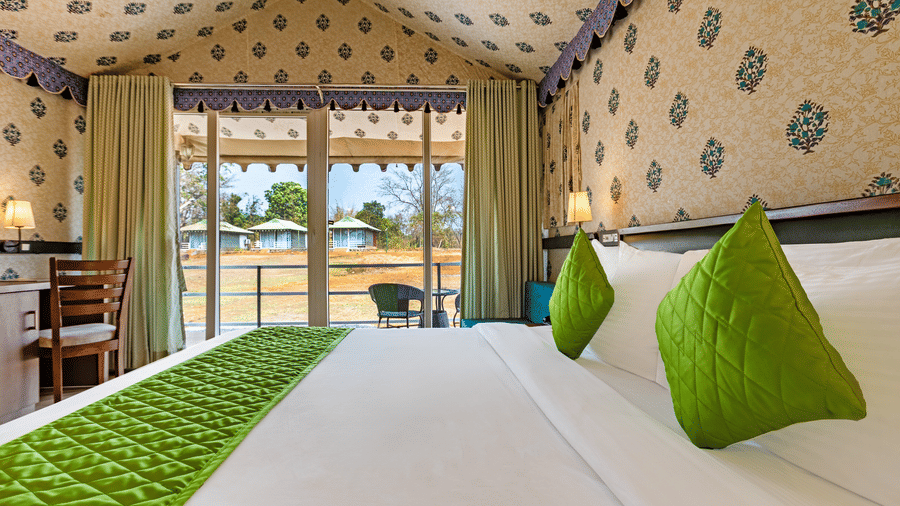 Nature Trails Kudalika premium AC tent double bed with green pillows and bedrunner, block-print fabric walls and ceiling, open glass door leading to private deck.