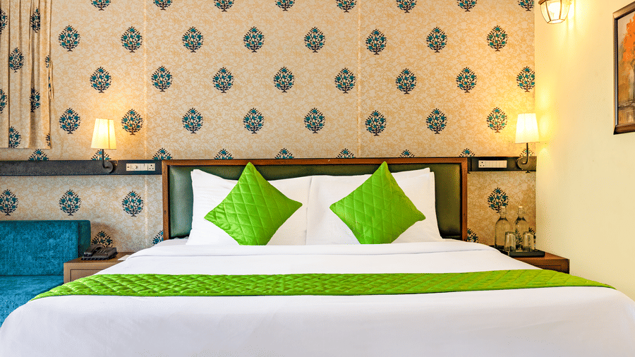 Nature Trails Kudalika premium AC tent double bed closeup with green quilted pillows, white bedding, green bedrunner, block-print headboard wall and brass wall lamps.