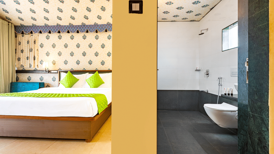 Nature Trails Kudalika premium AC tent showing double bed with green bedding and block-print fabric interior on left, bathroom with wall-hung WC visible on right.