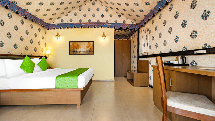 Nature Trails Kudalika premium AC tent room with double bed, green bedding, block-print fabric walls and ceiling, wooden work desk with chair and electric kettle.