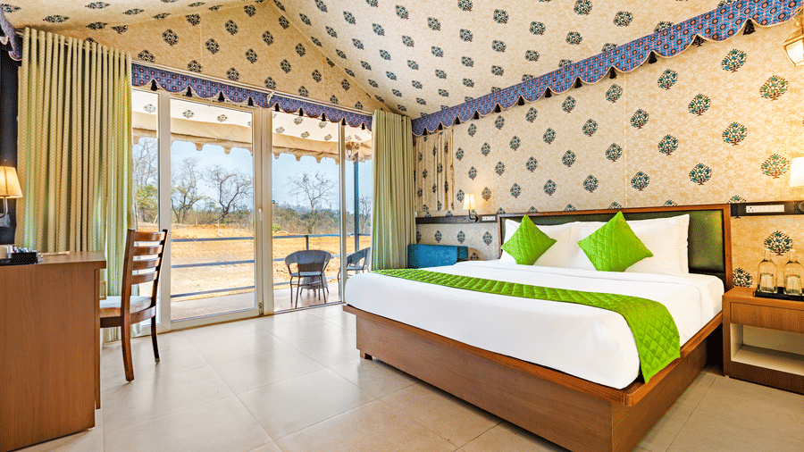 Nature Trails Kudalika premium AC tent room with double bed, green bedding, block-print fabric walls and ceiling, work desk, wooden wardrobe and open glass door.