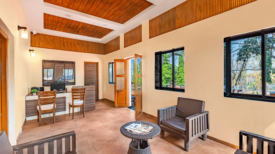 Nature Trails Kudalika reception interior with wooden front desk, computer, wooden lounge chairs, rattan coffee table, wood-panelled coffered ceiling and windows.