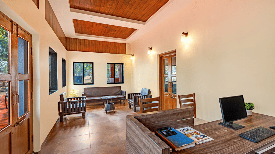 Nature Trails Kudalika reception desk with computer, keyboard, travel brochures, wooden counter, lounge seating in background and wood-panelled coffered ceiling.