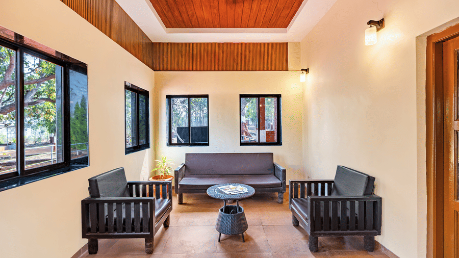 Nature Trails Kudalika reception waiting area with dark wood sofa set, rattan coffee table, multiple windows with garden views and wood-panelled coffered ceiling.