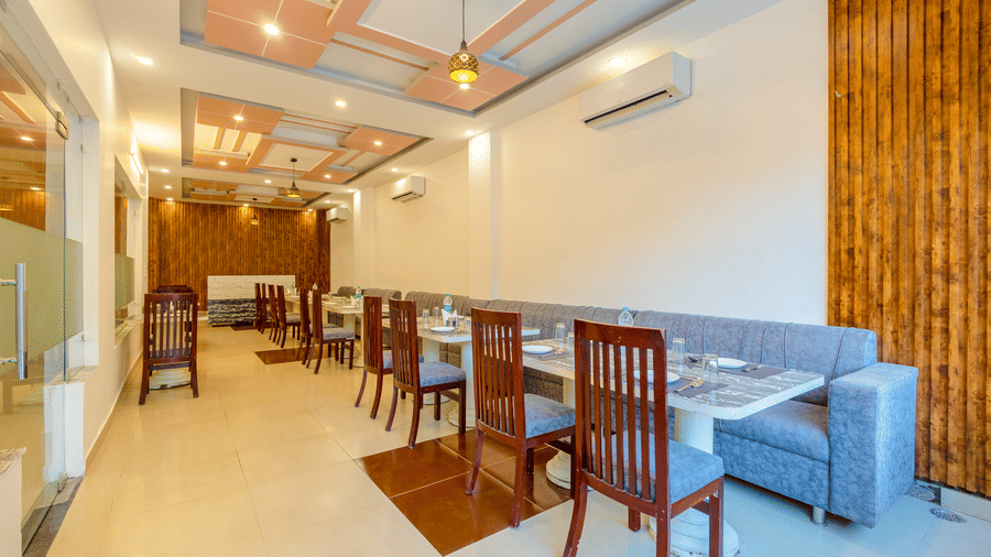 A bright and airy hotel dining hall with multiple wooden tables and a long grey sofa against the wall - Nature Trails Rishikesh