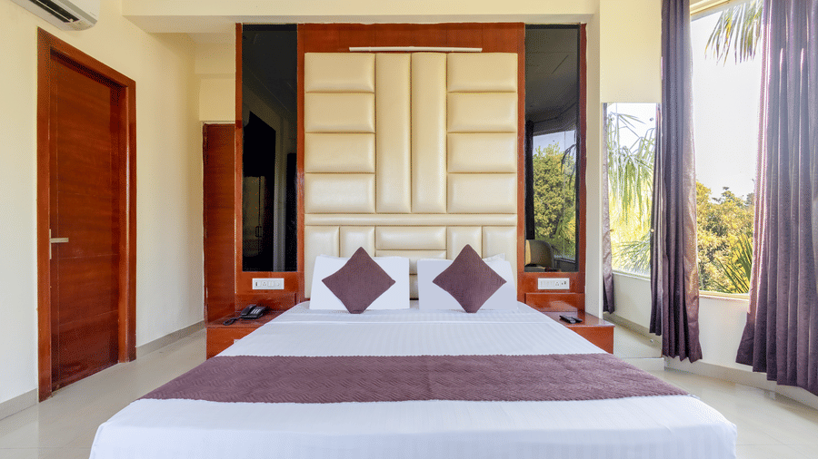 A modern hotel bedroom with a large cushioned headboard and purple decorative bed runners - Nature Trails Rishikesh