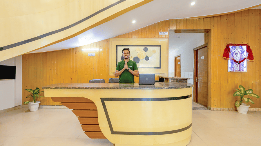A hotel staff member standing behind a modern, curved wooden reception desk in a well-lit lobby - Nature Trails Rishikesh