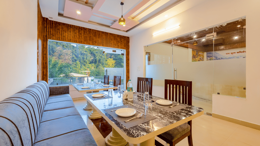 An indoor restaurant dining area with a marble-top table, wooden chairs, and a long upholstered bench - Nature Trails Rishikesh