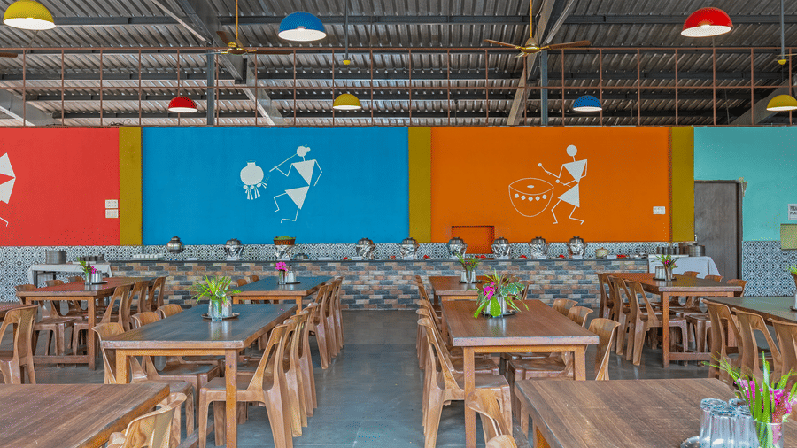 A resort dining area with wooden tables, vibrant blue, red and orange painted walls, hanging pendant lights and tribal art illustrations on walls.