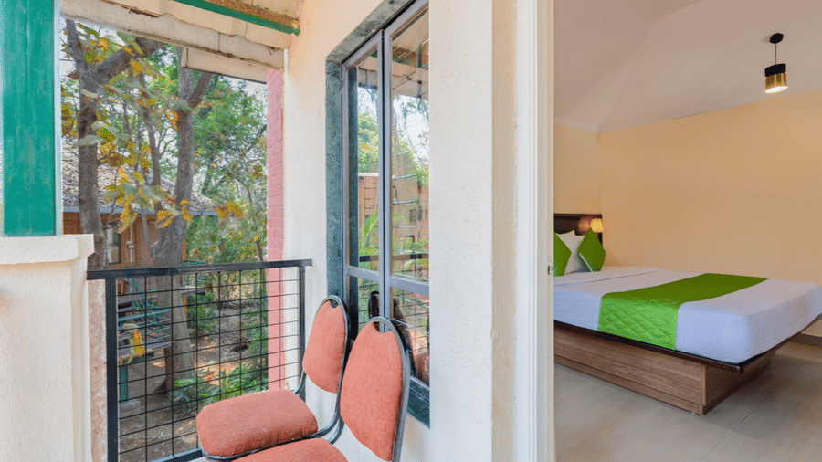 Bedroom with balcony access, double bed, and outdoor seating visible through the open door.