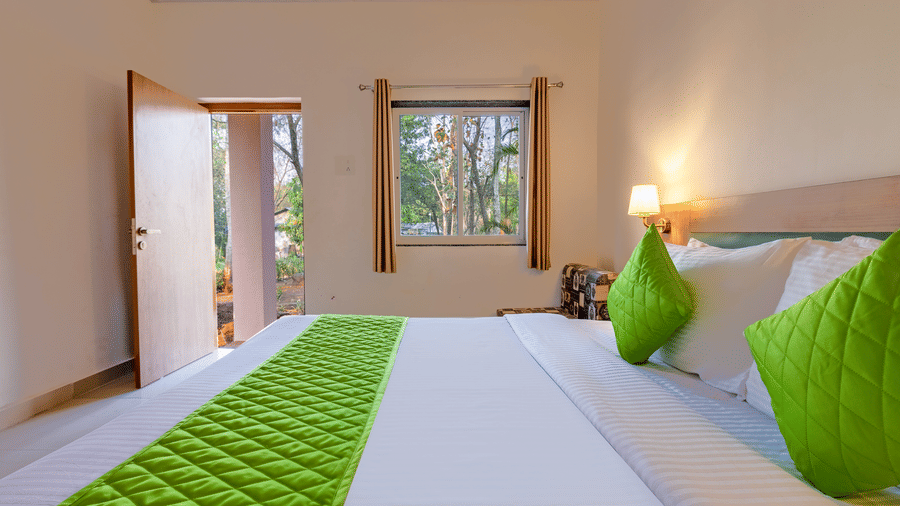 Angled view of a bedroom bed with green runner, open door, and window creating an airy feel.