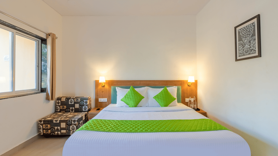 Bright bedroom with a double bed, green cushions, bedside lamps, and a window allowing natural light.