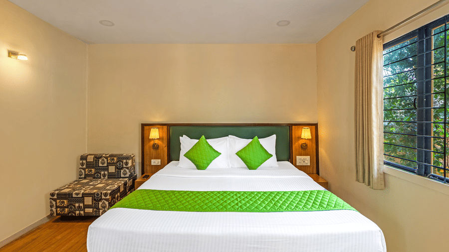 Comfortable bedroom with a double bed, green cushions, bedside lighting, and a large window with outdoor greenery view.