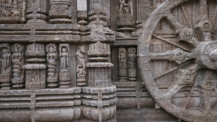 Intricately carved stone wheel on the Sun Temple wall, surrounded by detailed reliefs, decorative motifs, and finely chiselled architectural elements.