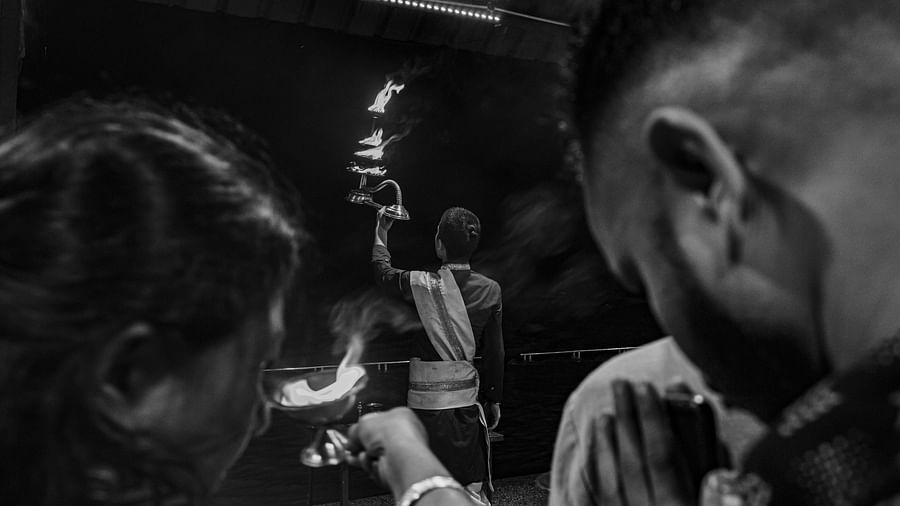 A black and white image of a priest performing aarti with people behind praying.