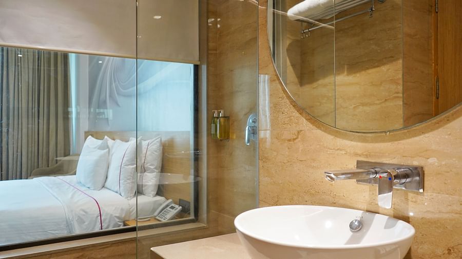 A view of a room from the bathroom with a large window allowing natural light and a comfortable bed.