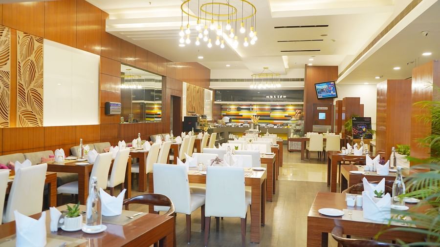 A side angle view of the restaurant interior at Nemesia featuring chandeliers, wooden furniture, tables arranged with napkins, water glasses, and plates.