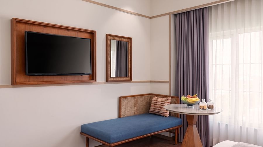 A hotel bedroom with a bed, a seating area, and a TV.
