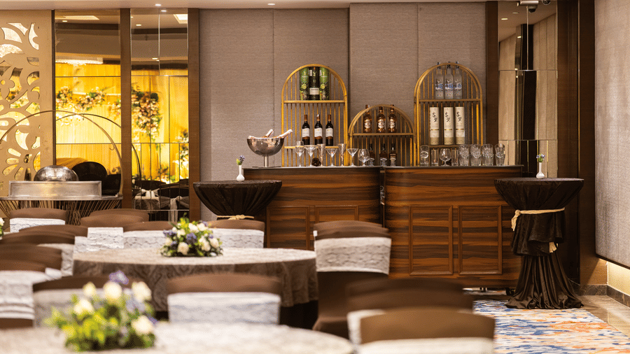 A bar counter setup at Nirvana Sarovar Portico, Gorakhpur featuring high tables, stool seating, and bottles displayed on shelves. 