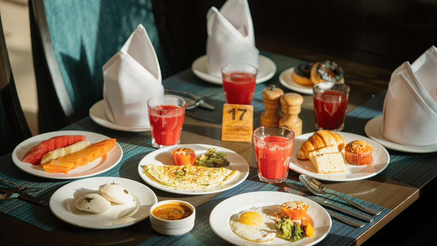 A breakfast table at Nirvana Sarovar Portico, Gorakhpur featuring plates of fruit, eggs, pastries, and fresh juices.