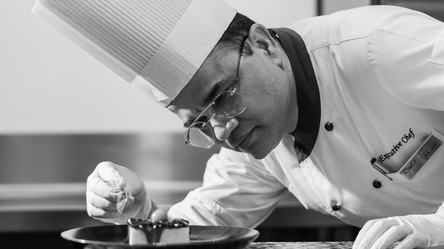 A chef at Nirvana Sarovar Portico, Gorakhpur carefully decorating a dessert dish on a dark plate.