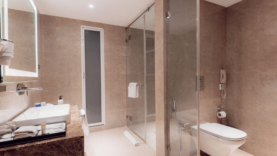 A spacious bathroom at Nirvana Sarovar Portico, Gorakhpur featuring a walk-in glass shower enclosure, vanity mirror, and toilet area.