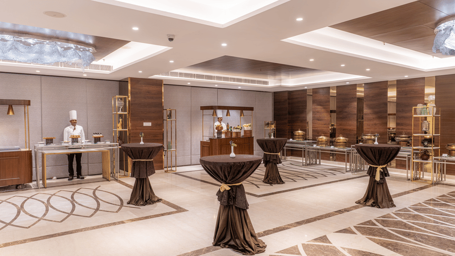 An indoor event space at Nirvana Sarovar Portico, Gorakhpur featuring tall cocktail tables and live cooking counters.