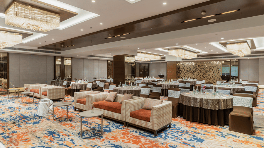 An event space at Nirvana Sarovar Portico, Gorakhpur featuring sofas, round tables, and dressed chairs.