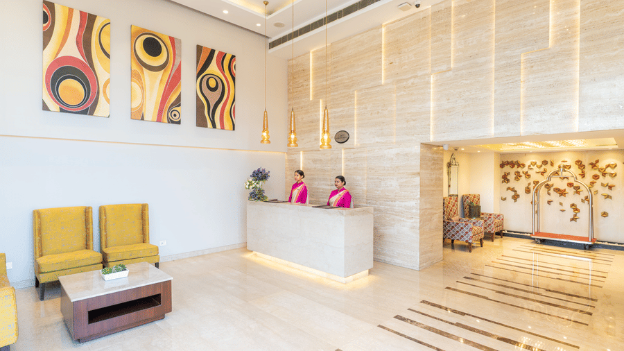 The front desk reception at Nirvana Sarovar Portico, Gorakhpur featuring staff members, seating area, abstract wall art, and luggage cart.