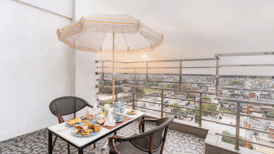 A balcony seating setup at Nirvana Sarovar Portico, Gorakhpur featuring 2 chairs, a table with an umbrella, and city views.