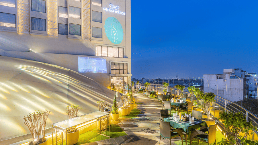 A rooftop seating area at Nirvana Sarovar Portico, Gorakhpur featuring outdoor tables, potted plants, and city views.