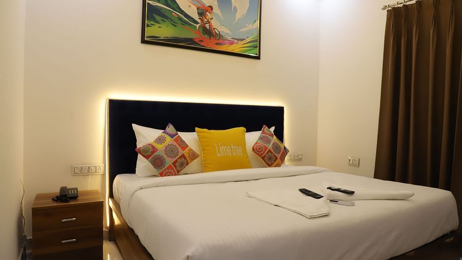A room featuring a well made bed with vibrant pillows a wall painting and a side drawer - Opulent Inn