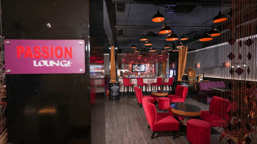 Interior of Passion Lounge at Park Plaza Ludhiana featuring red upholstered seating dark wooden flooring a glowing pink neon sign and warm ambient ceiling lighting.