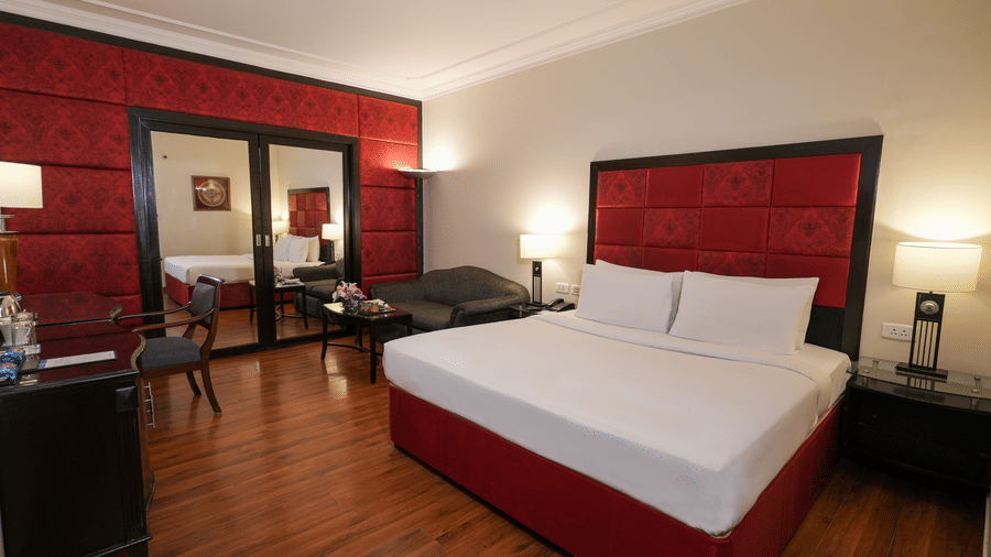 A room at Park Plaza Ludhiana featuring a king bed with white bedding bold red wall panels dark wooden flooring bedside lamps and a seating area near the window.