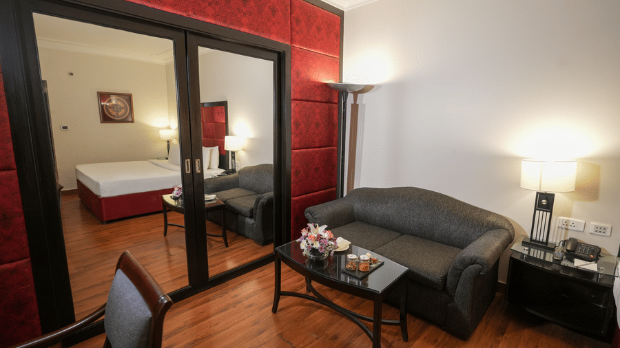A sitting area at Park Plaza Ludhiana featuring a grey sofa dark wooden flooring large mirror panels red accent wall and warm ambient lighting in a modern setting.