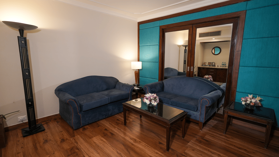 A sitting area at Park Plaza Ludhiana featuring two blue sofas teal accent wall dark wooden flooring a floor lamp and a large mirror near the doorway.