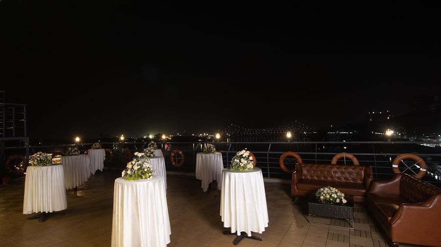Outdoor rooftop setting with round tables covered in white, decorative flower arrangements, and a night view.