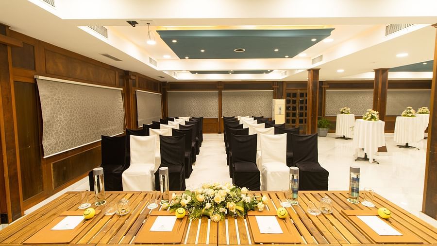 Spacious conference room arranged with comfortable seating and tables for a formal event, showcasing warm lighting and wooden elements.