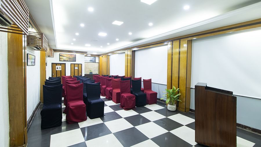 Functional seminar room with black and red covered chairs, checkered floor, and white projector screens for presentations.